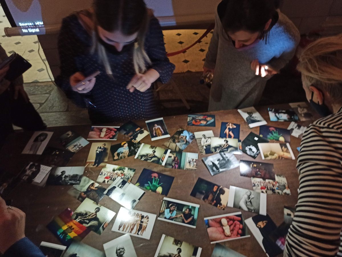 radionica REWOMEN na kojoj su žene okupljene oko stola na kojem se nalaze razbacane fotografije