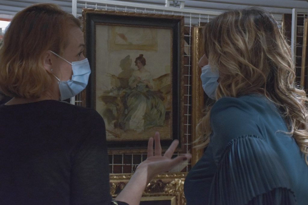 two women looking at the paintings with masks on their faces and commenting